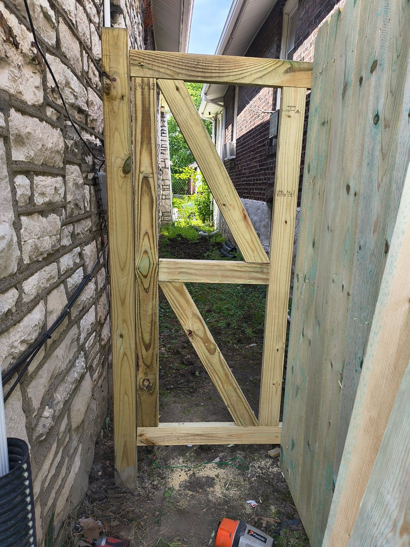 Pressure-treated fence gate frame being built beside a stone wall
